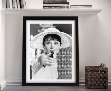 A framed canvas print of Audrey Hepburn Gun hanging on a wall, showing a woman in a wide‑brimmed hat pointing a small gun towards the viewer, ideal as a romantic or anniversary portrait gift.
