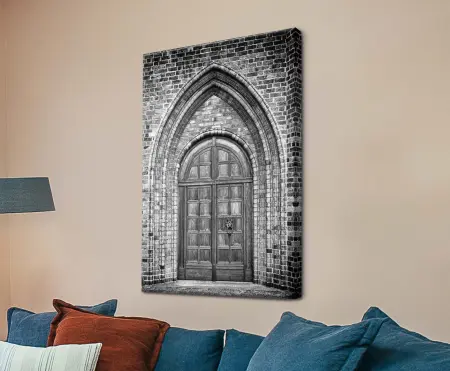 A canvas print showing a stone archway and wooden church door in black and white, with visible texture in the brickwork and door panels.