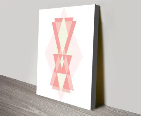 Pink geometric canvas print with overlapping triangles in blush, coral and cream tones leaning against a grey wall