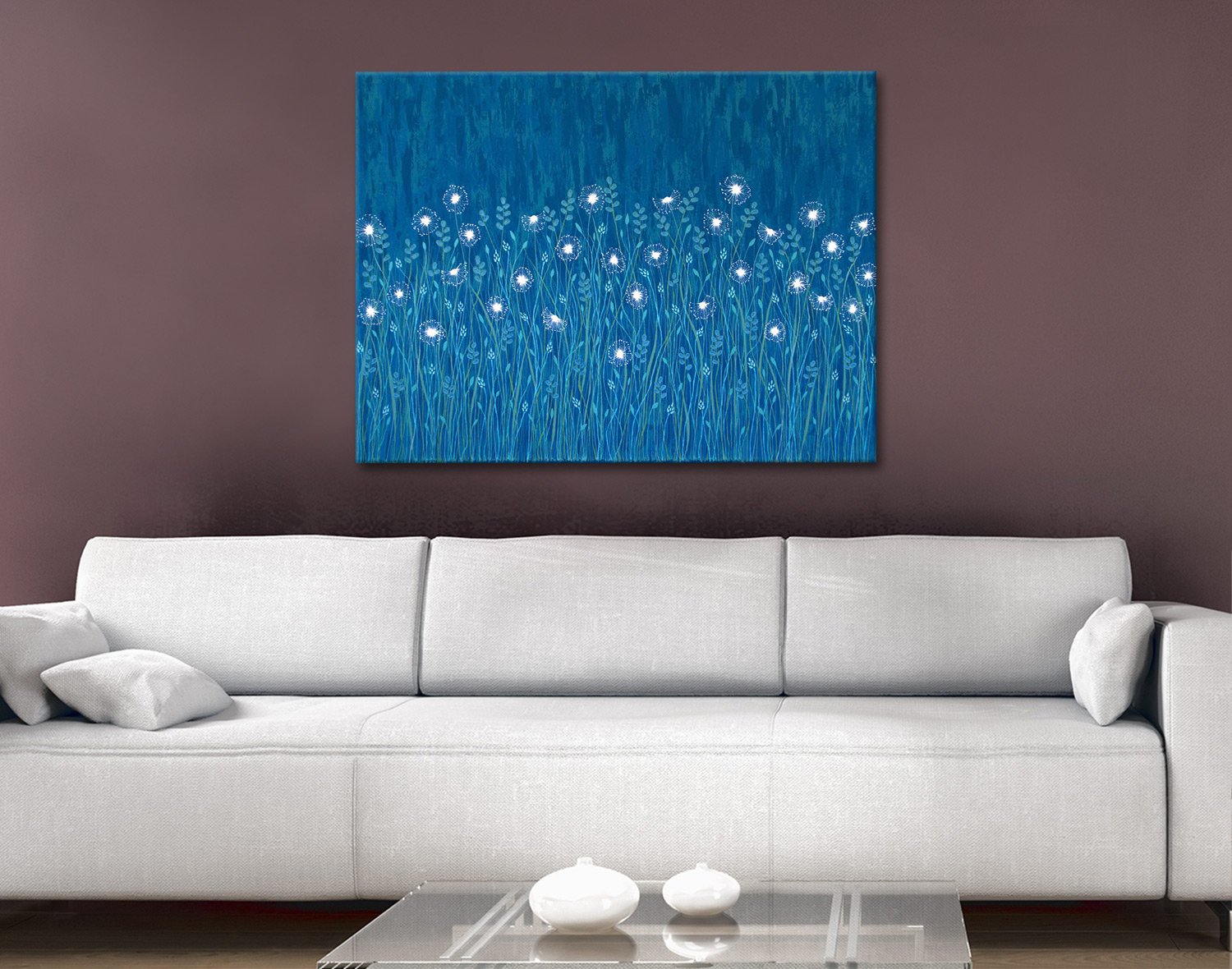Blue canvas print of glowing white dandelions in tall grass hung above white sofa in burgundy living room