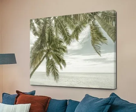 A canvas print showing two tall palms stretching over a calm, pale ocean with soft clouds drifting across the sky.