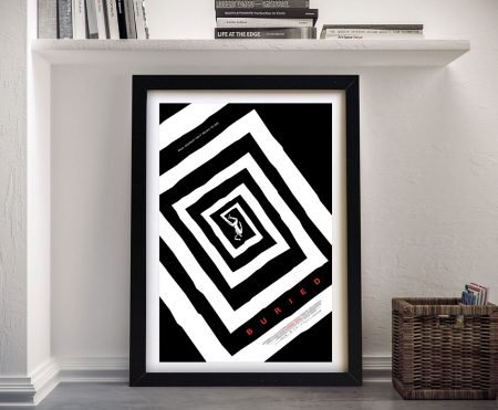 Framed Buried movie poster with black and white spiral design leaning against a white wall beside a wicker basket