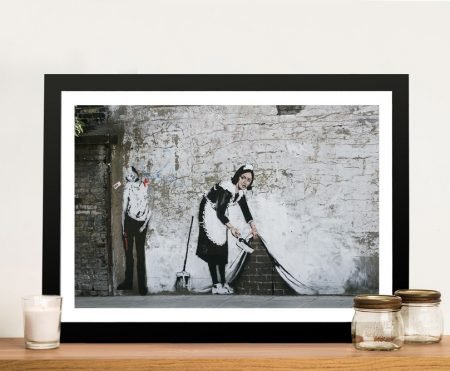 Framed Banksy maid stencil lifting a brick wall to sweep beneath