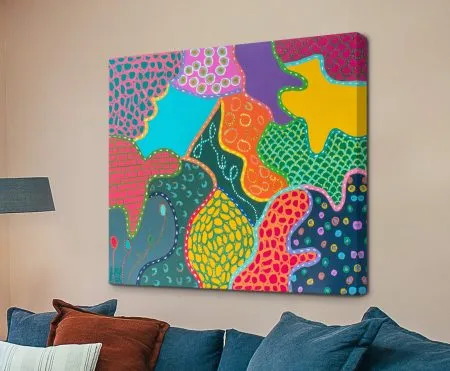 Vibrant abstract canvas print I'm Cheery by Helen Joynson with pink, yellow and teal patterned shapes above blue sofa