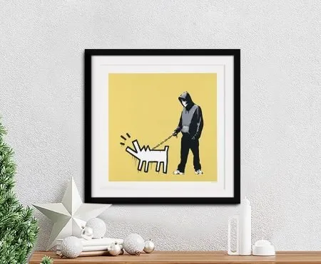 Banksy Choose Your Weapon framed print in pale yellow, hooded figure with a barking dog