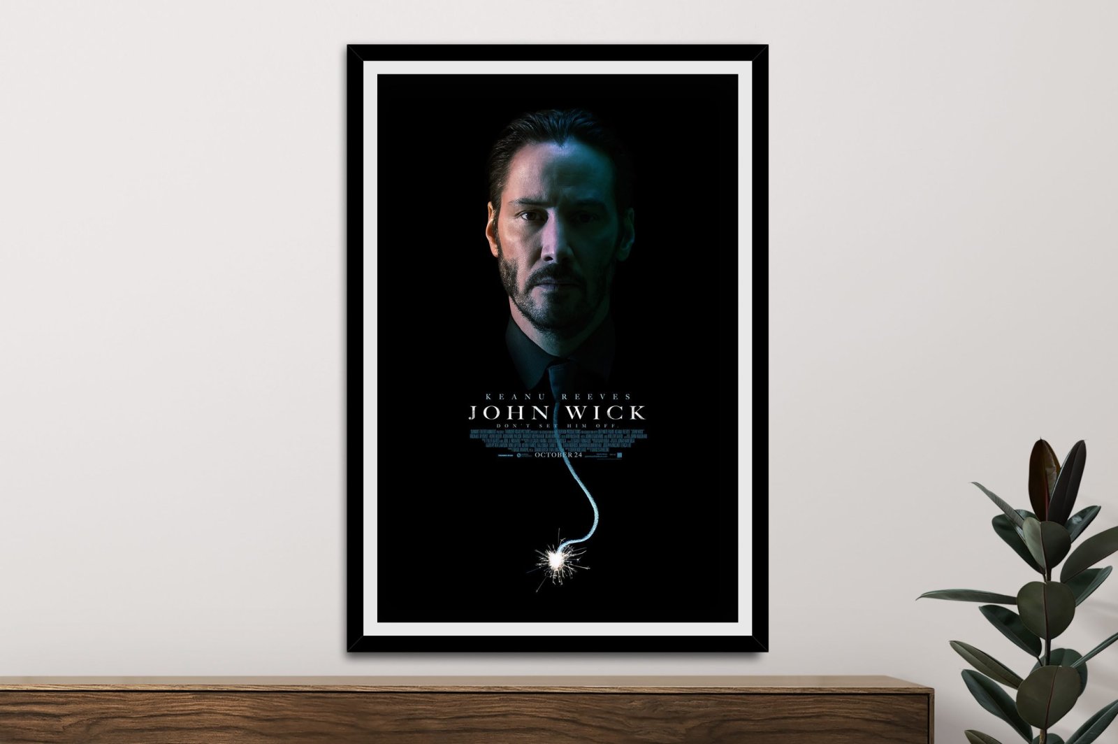 Framed John Wick movie poster featuring Keanu Reeves on black background, mounted on white wall above timber console