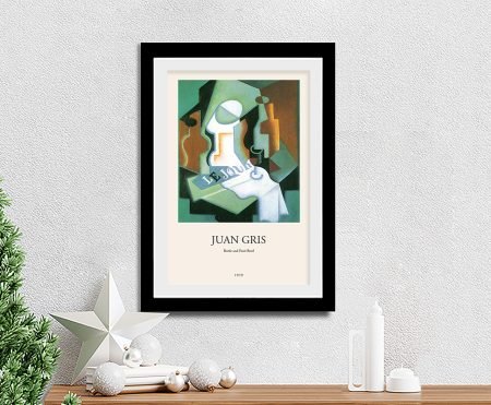 Juan Gris Bottle and Fruit Bowl modern art print in a black frame on a soft white wall above a pine console with festive ornaments