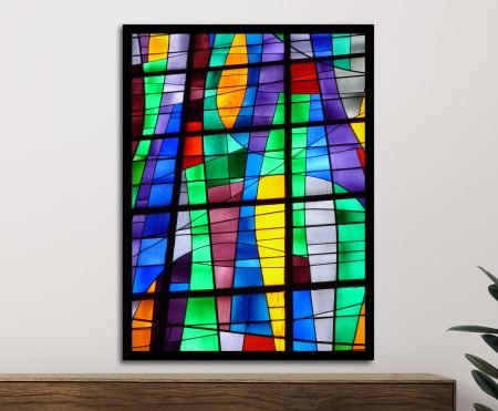 Vibrant stained glass abstract framed print in black frame above wooden sideboard, featuring green, purple, blue and yellow panels