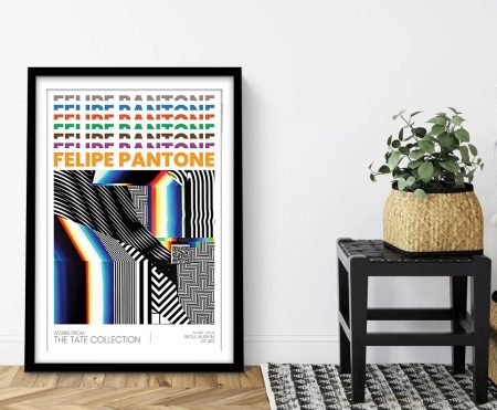 Felipe Pantone Optichromias exhibition poster framed in black, leaning against white wall beside woven planter on stool
