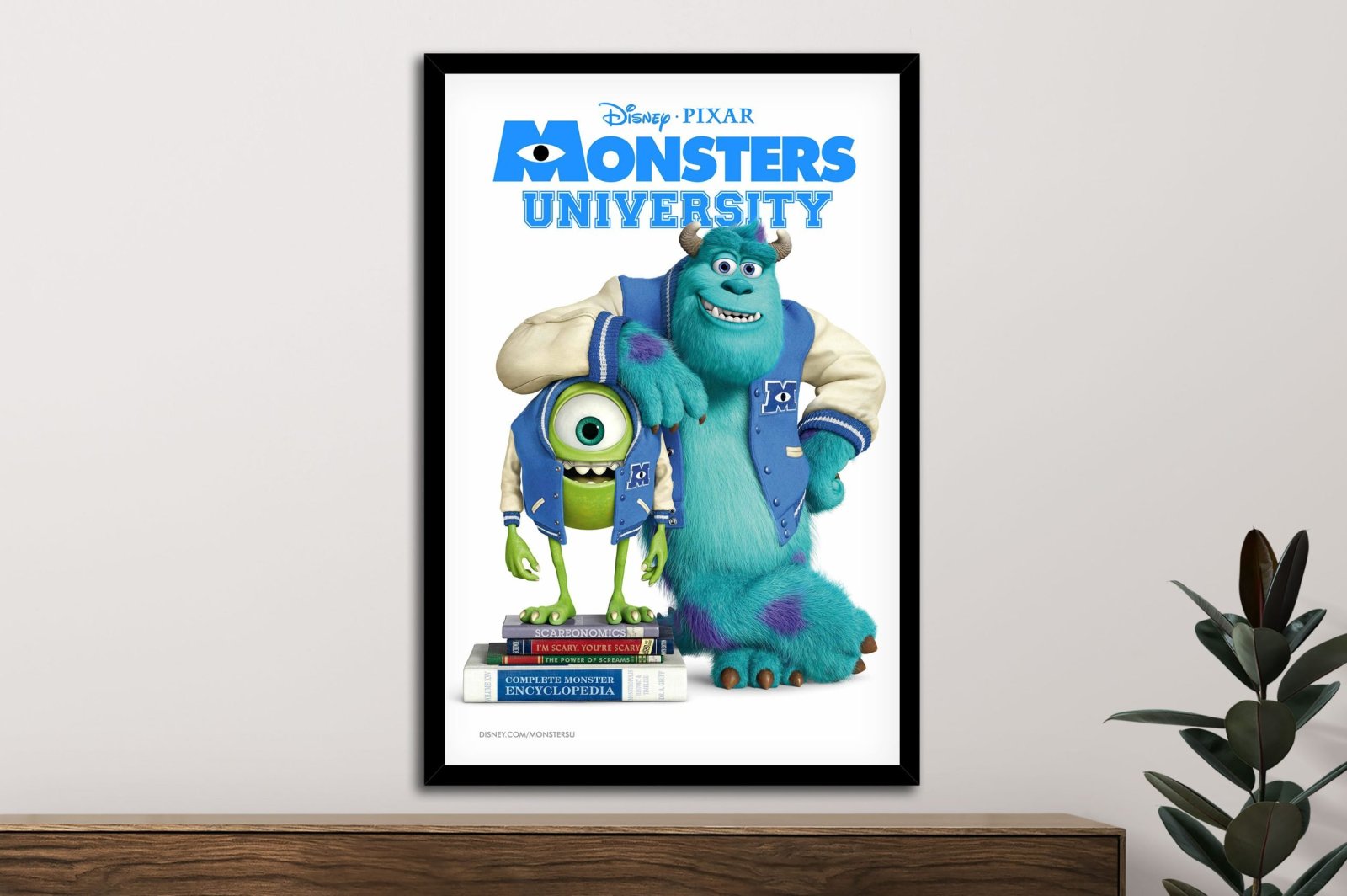 Framed Monsters University movie poster featuring Mike and Sulley in blue varsity jackets above a wooden console