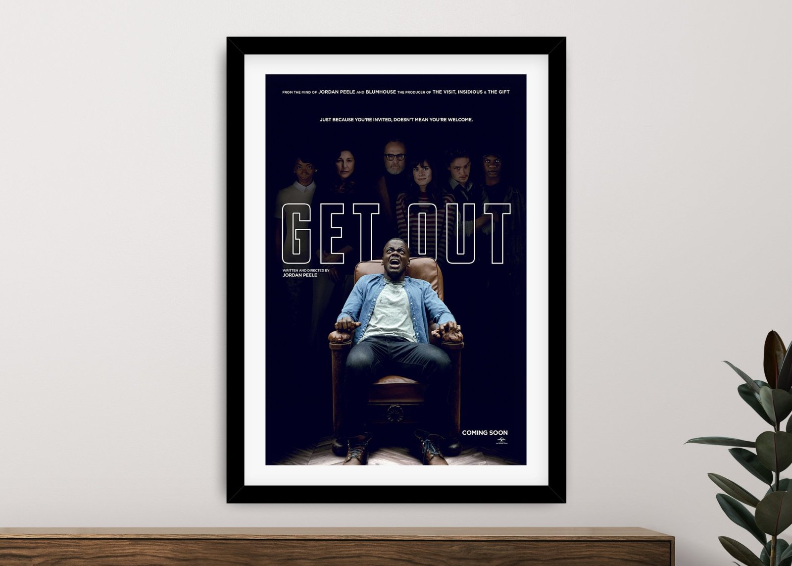 Get Out movie poster framed print featuring Daniel Kaluuya in chair, hung on light grey wall above timber console